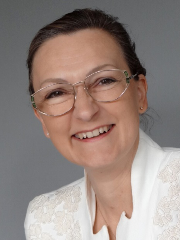 Portraitfoto von Regina Mihal, mit Brille, weißer Spitzenbluse, zusammengebundenen Haaren und einem bezaubernden Lächeln